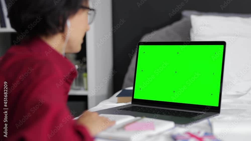 Mature woman in eyewear and earphones having online studying on modern laptop at home. Caucasian female sitting at bedroom and looking on computer with green empty screen. Mature woman in eyewear and earphones having online studying on modern laptop at home. Caucasian female sitting at bedroom and looking on computer with green empty screen.