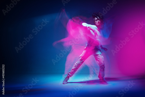 Dancing mixed race girl in colourful neon studio light. Female dancer show expressive hip hop dance. Long exposure