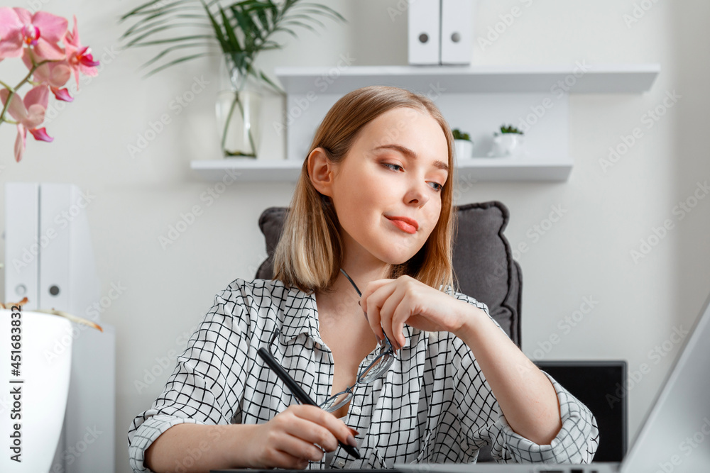 Young woman freelance graphic designer working using graphic tablet and laptop in home office interior. Caucasian Blonde Confident focused woman doing writing paper work using laptop. Young woman freelance graphic designer working using graphic tablet and laptop in home office interior. Caucasian Blonde Confident focused woman doing writing paper work using laptop.