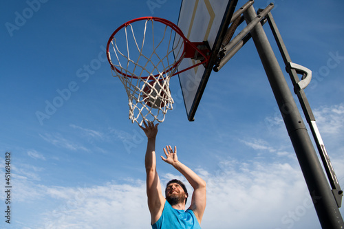 Basketball player. Sports and basketball. A young man jumps and throws a ball into the basket. Blue sky and court in the background.