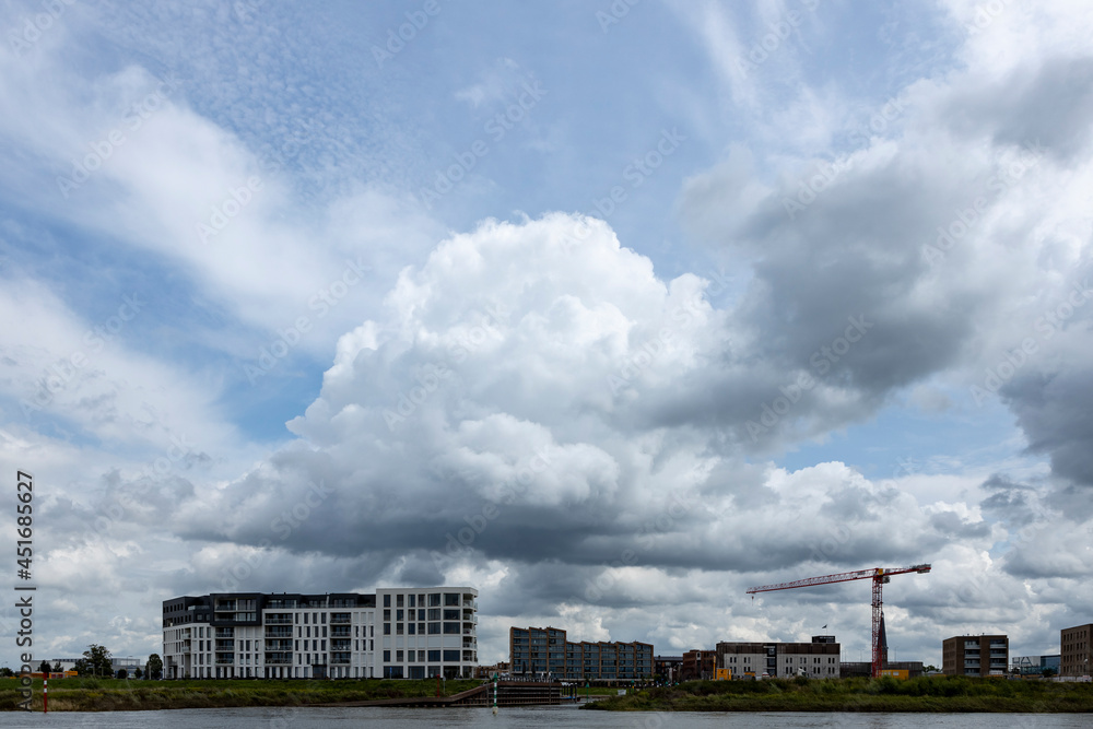 Exterior facade of newly build luxury apartment building Kade Noord next to construction site of Kade Zuid with river IJssel in the foreground and large cumulus raincloud above Exterior facade of newly build luxury apartment building Kade Noord next to construction site of Kade Zuid with river IJssel in the foreground and large cumulus raincloud above