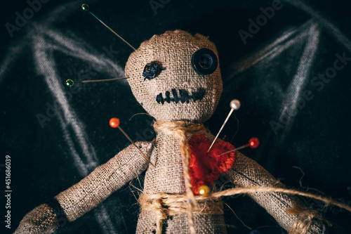 Voodoo rag doll with buttons instead of eyes and studded with needles, close-up top view.