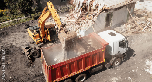 Excavator bucket loads industrial debris into truck. Process of demolishing and destruction old house. Release of quarters for new development. photo