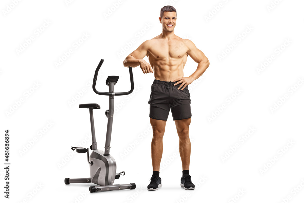 Fitness trainer posing shirtless and leaning on an exercise bike Fitness trainer posing shirtless and leaning on an exercise bike