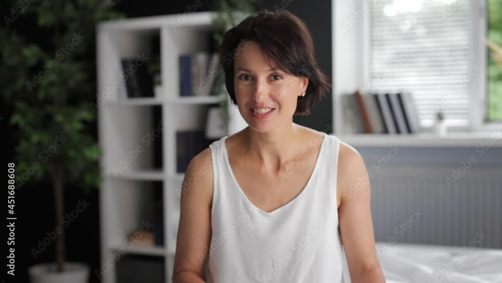 Portrait of positive mature woman in pajamas sitting on bed and talking on camera. First person view. Recording of video vlog. Female blogger at home. Portrait of positive mature woman in pajamas sitting on bed and talking on camera. First person view. Recording of video vlog. Female blogger at home.