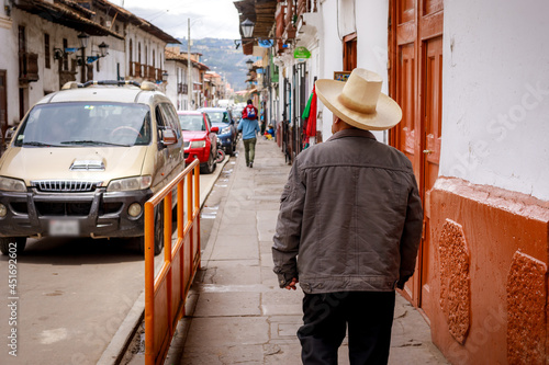 A Peruvian man wearing a traditional hat walking down the street in the city center of Cajamarca in Peru photo