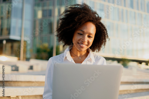 A smart student in a white afro shirt looks smiling. A confident female manager works near the office in a cafe. Prints a message in the messenger to the client by mail.