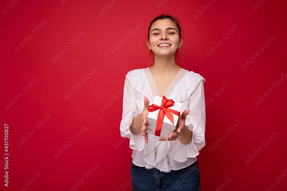Shot of attractive positive smiling young brunette woman isolated over colourful background wall wearing everyday trendy outfit holding gift box and looking at camera Shot of attractive positive smiling young brunette woman isolated over colourful background wall wearing everyday trendy outfit holding gift box and looking at camera