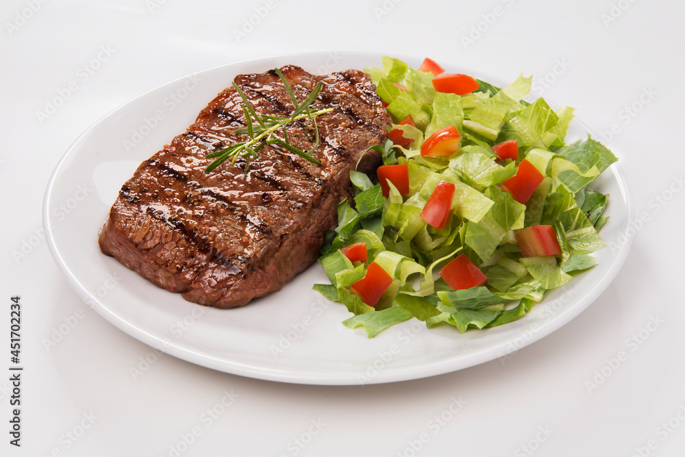 Delicioso corte de carne bovina grelhada com salada de alface picada com tomate e pepino. No fundo branco para recorte. Delicioso corte de carne bovina grelhada com salada de alface picada com tomate e pepino. No fundo branco para recorte.