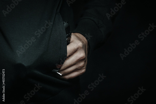 Person is threatening with gun in his jacket pocket. Thief hides weapon in clothes. Night criminal and robber. Close up of murderer. © Konstantin Savusia