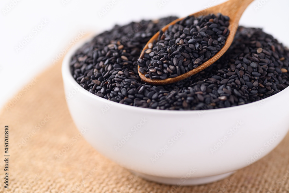 Black sesame seeds in a white bowl with wooden spoon, Food ingredients Black sesame seeds in a white bowl with wooden spoon, Food ingredients