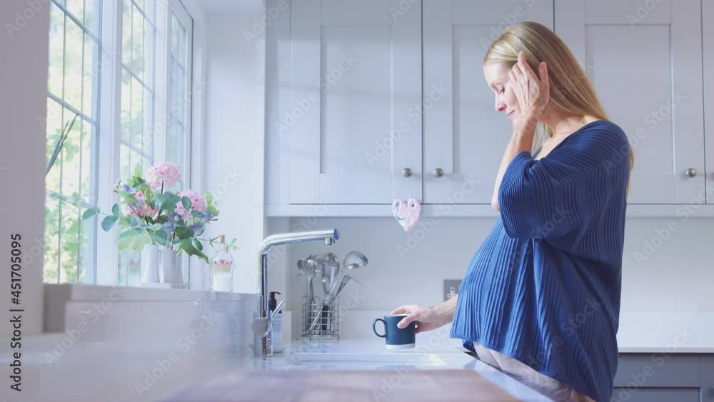 Pregnant mature woman at home with hot drink standing by kitchen window - shot in slow motion Pregnant mature woman at home with hot drink standing by kitchen window - shot in slow motion