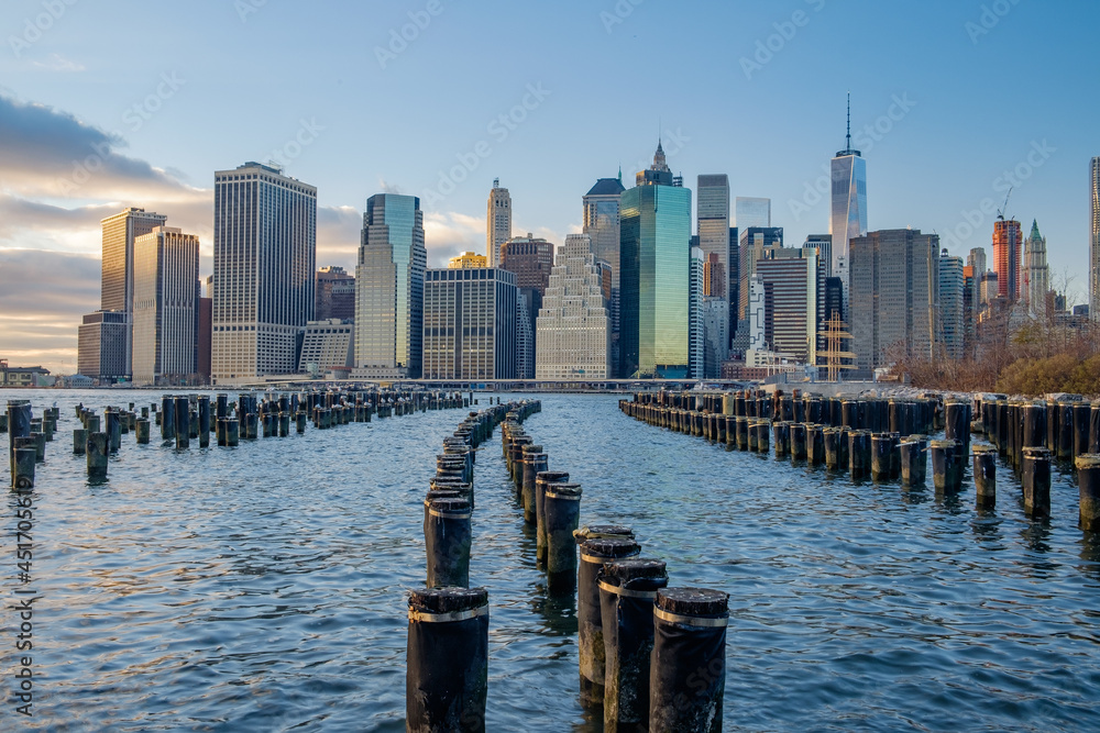 Old Wooden Pilings on the East River reflect the sunset as the lower New York City Manhattan Financial district lights begin to turn on Old Wooden Pilings on the East River reflect the sunset as the lower New York City Manhattan Financial district lights begin to turn on