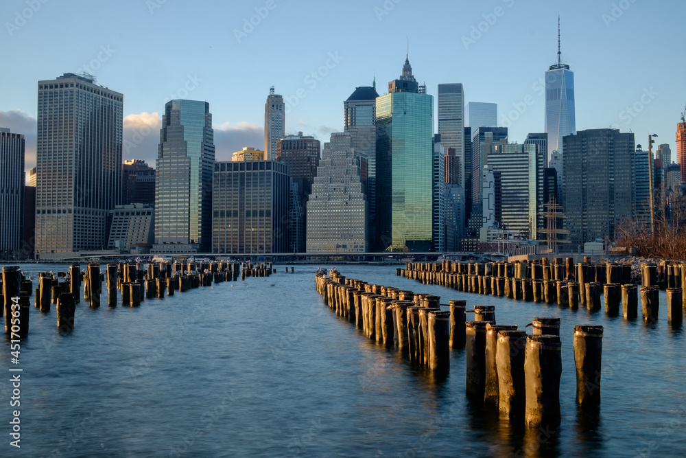 Old Wooden Pilings on the East River reflect the sunset as the lower New York City Manhattan Financial district lights begin to turn on