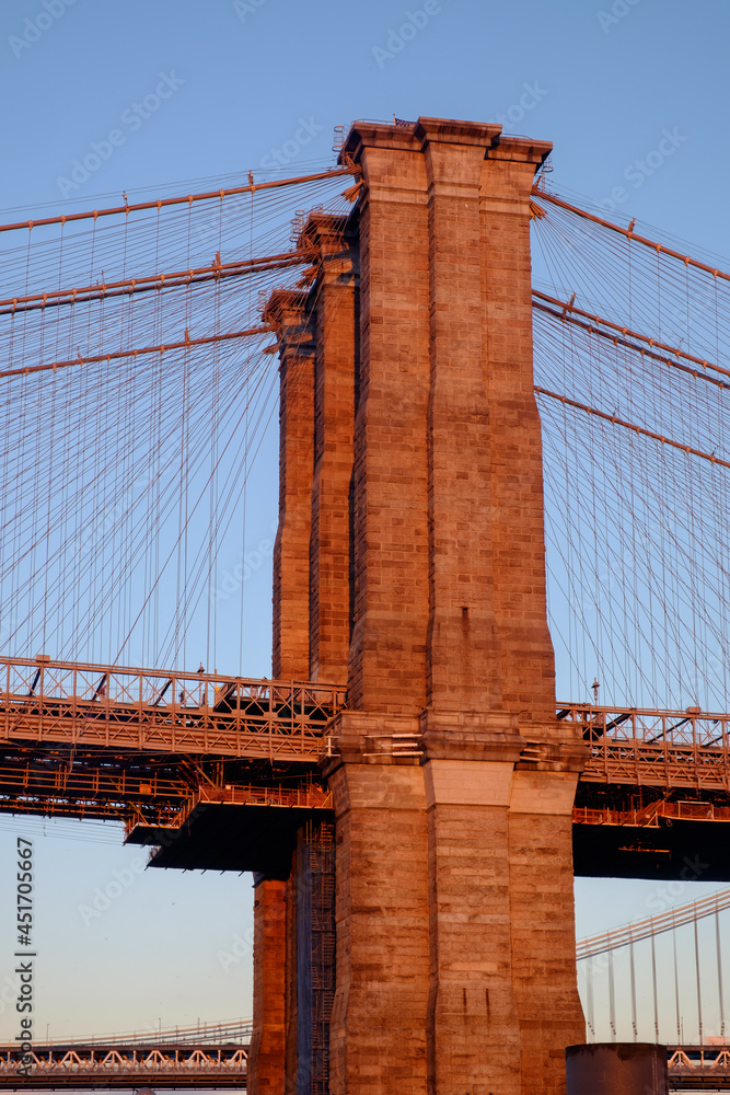 Fototapeta premium One of the towers of the famous old and historic Brooklyn Bridge spanning the East River from Manhattan into Brooklyn as seen at sunset
