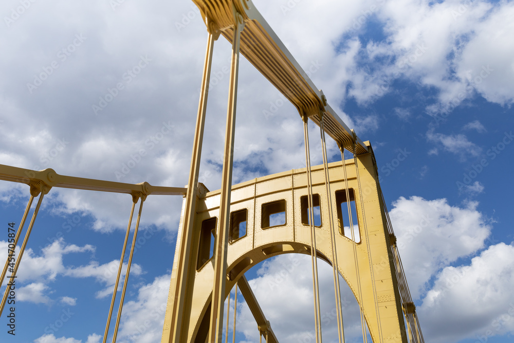 Bright sunlight on the upright structure of a yellow self anchored suspension bridge, deep blue sky with clouds, horizontal aspect