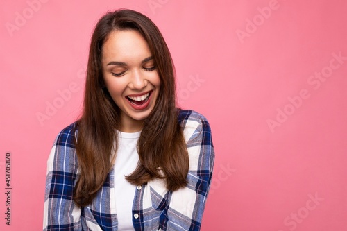 Photo portrait of young beautiful smiling hipster brunette woman in trendy blue and white shirt and jeans clothes. Sexy carefree female person posing isolated near pink wall with empty space in studio © Ivan Traimak