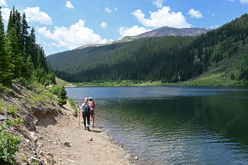 Two young female hikers on shore of Upper Urad Reservoir on Hassell Lake Trail in Arapaho National Forest, Colorado on sunny summer afternoon.