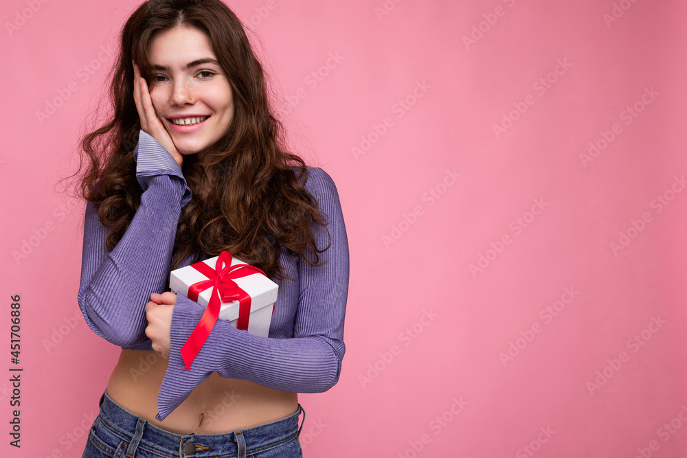 Beautiful happy young brunette woman isolated over colourful background wall wearing stylish casual clothes holding gift box and looking at camera Beautiful happy young brunette woman isolated over colourful background wall wearing stylish casual clothes holding gift box and looking at camera