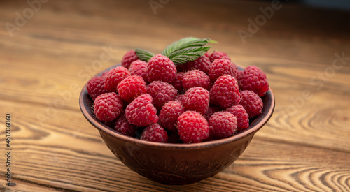 Bowl with fresh ripe delicious raspberries and a green leaf on a wooden background