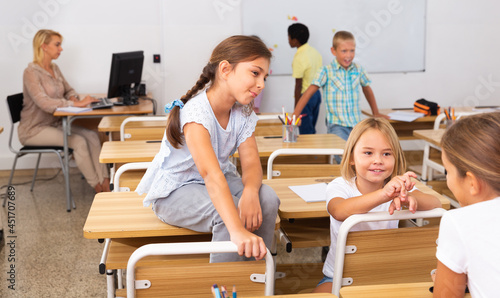 Girl and boy are sitting at the desk and talking about life in the classroom