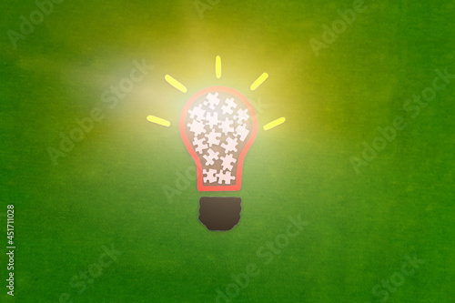Obraz na płótnie Electric light bulb, puzzle pieces on a green background. The concept of the development of creative ideas. w salonie