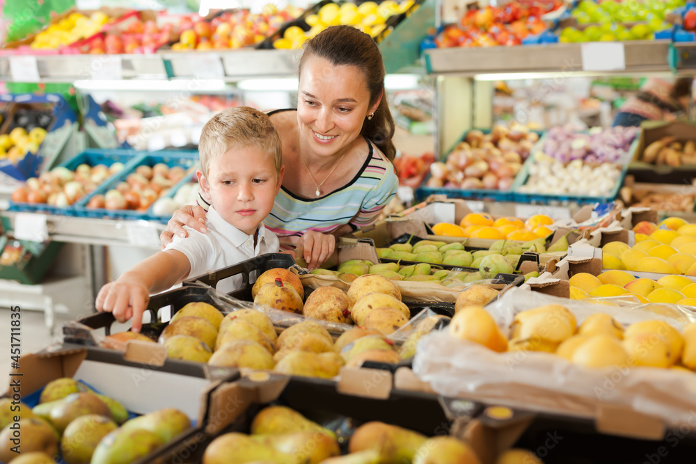 Positive boy with his mother choosing fresh pears and apples at fruit department of supermarket