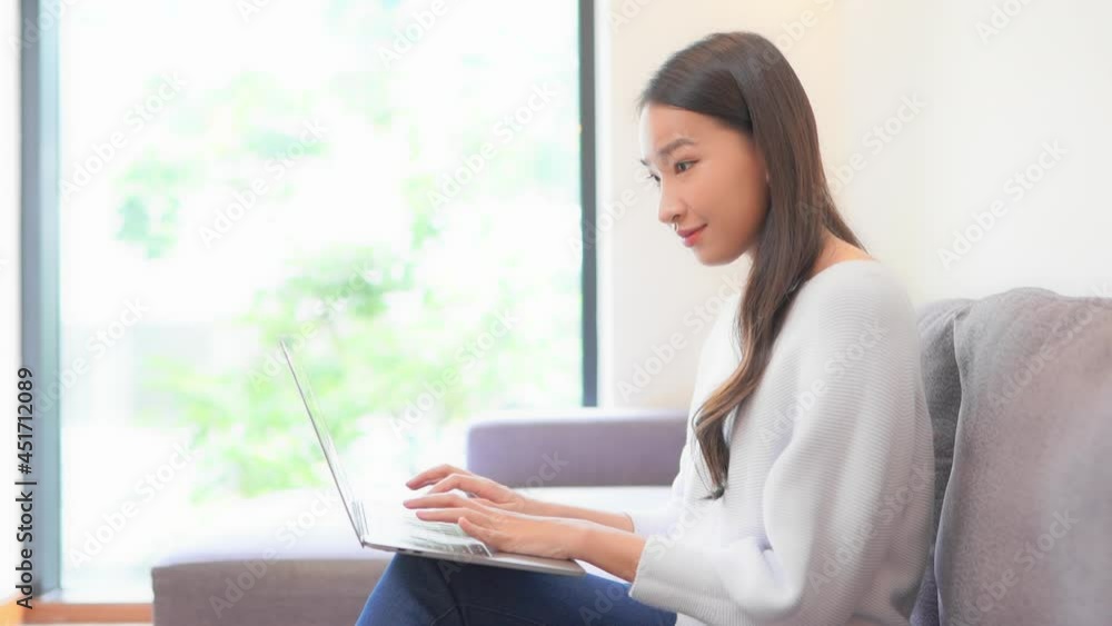 Portrait of Asian woman sitting on sofa near window typing on a laptop computer. Lady communicating on the Internet. Work from home, remote office, business concept. Portrait of Asian woman sitting on sofa near window typing on a laptop computer. Lady communicating on the Internet. Work from home, remote office, business concept.