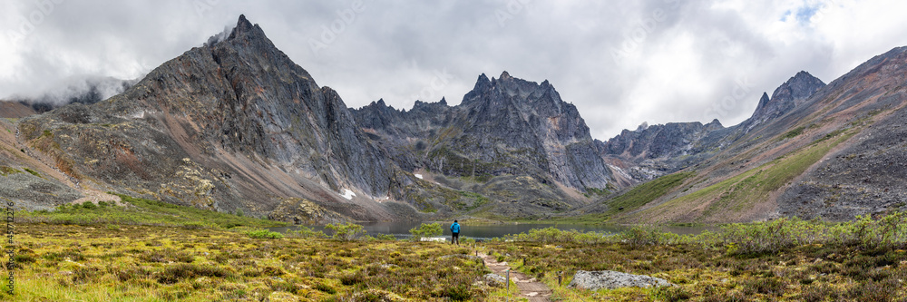 Backcountry camping area of Tombstone Territorial Park off Dempster Highway during summertime on a cloudy morning from the Grizzly Lake hiking trail with hiker in blue jacket. 