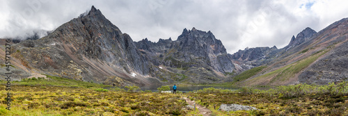 Backcountry camping area of Tombstone Territorial Park off Dempster Highway during summertime on a cloudy morning from the Grizzly Lake hiking trail with hiker in blue jacket. 