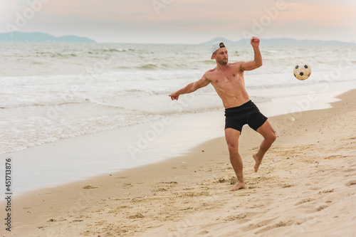 Caucasian young man playing beach soccer at summer on tropical city