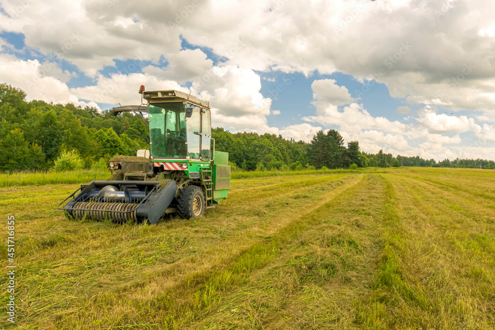 Fototapeta premium combine harvester gathering harvest on a agricultural field with cloudy sky and green forest on thr background , farm rural landscape
