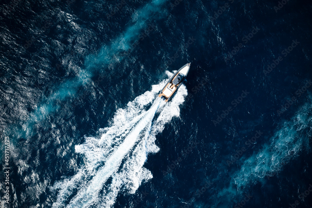View from above, stunning aerial view of a boat cruising on a blue water creating a wake.Sardinia, Italy.