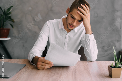 Billede på lærred Worker or businessman with sick headache reads contract or bankruptcy documents