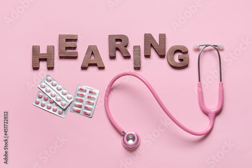 Word HEARING with stethoscope and pills on color background