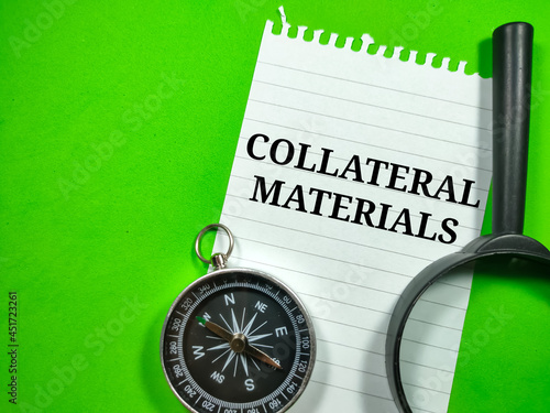 Business concept.Text COLLATERAL MATERIALS writing on notepaper with magnifying glass and compass on a green background.