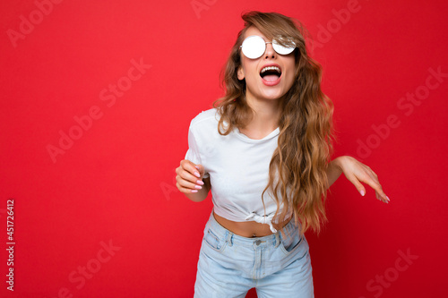 Slika na platnu Shot of beautiful amusing joyful young dark blonde curly woman isolated over red
