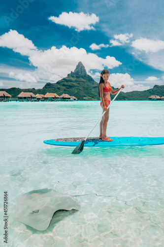 SUP Stand-up paddle board woman wwimming with stingrays tourist tour activity happy Asian woman on Bora Bora island beach at Tahiti overwater bungalow hotel, holiday travel vacation. photo