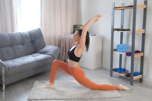 Young woman is practicing warrior pose I virabhadasana doing yoga at home. Sport fitness training stretching workout yoga wellness concept. Concentration flexibility energy concept, standing asana. photo