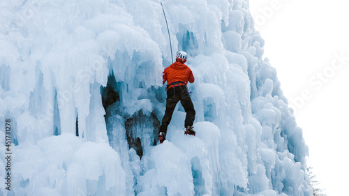 Aerial shot of a frozen ice waterfall, and the male climber progresses up the slope, while rope attached to his harness prevents him from falling