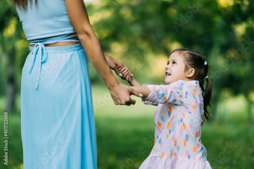 Toddler girl holding hands with her young mother outside