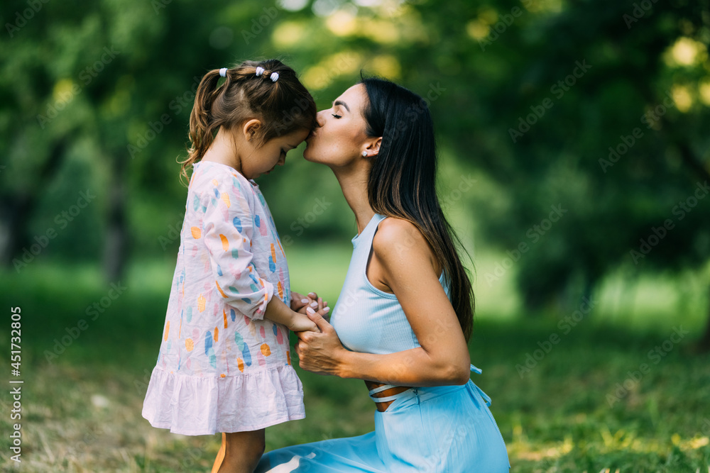 Little girl kissing her mother in a green park
