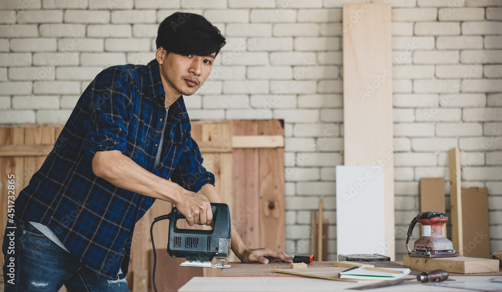 Portrait of good looking Asian carpenter working for DIY jobs in carpenter room with several kinds of woods and types of equipment