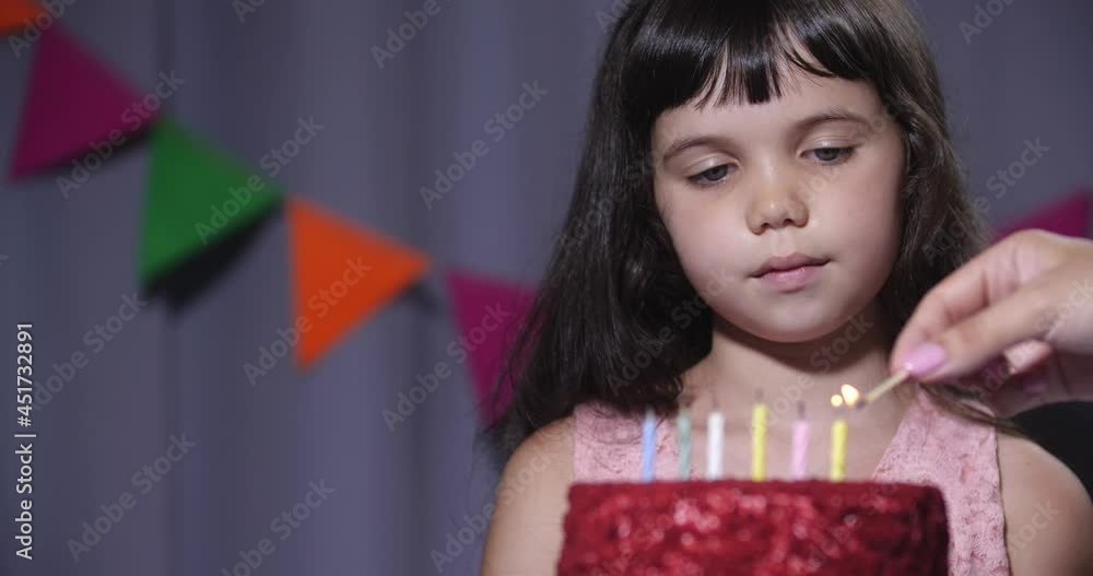 Close-up portrait with copy space of six years old girl sitting near a birthday cake with candles. Mom's hand lighting candles, daughter blowing them out and clapping her hands. Slow motion 4k 50 fps Close-up portrait with copy space of six years old girl sitting near a birthday cake with candles. Mom's hand lighting candles, daughter blowing them out and clapping her hands. Slow motion 4k 50 fps