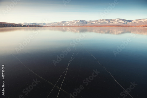 Thin ice on the lake in the early winter. Mountains and their reflections in the ice surface of the lake. Beautiful winter landscape. South Ural, Bashkortostan, Russia