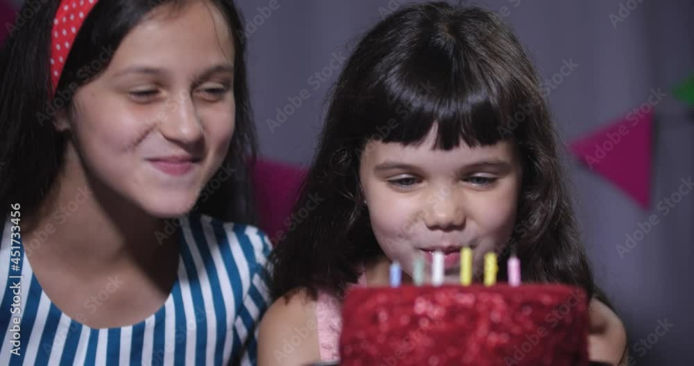Two girls are sitting near a birthday cake with candles and eagerly want to take a bite of it. 50 fps slow motion 4k Two girls are sitting near a birthday cake with candles and eagerly want to take a bite of it. 50 fps slow motion 4k