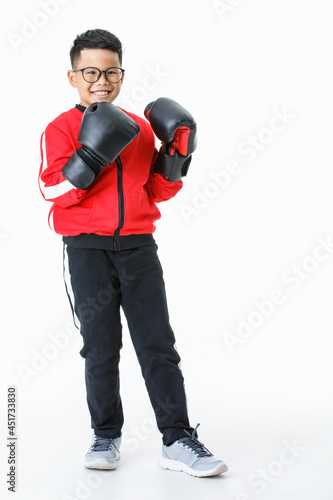 Lovely cutout portrait of young healthy Asian boy wearing red jacket, black pants, and boxer gloves standing tight and ready to fight strongly with happily smiling as enjoy boxing practice