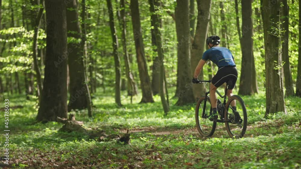 A cyclist quickly passes through a forest road. He is making a quick sprint. He is going around fallen trees. The camera is moving from right to left and follows him. 4K A cyclist quickly passes through a forest road. He is making a quick sprint. He is going around fallen trees. The camera is moving from right to left and follows him. 4K
