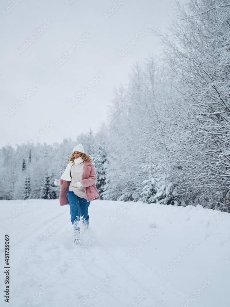 Portrait of young smiling woman walking in winter forest wearing white knitted hat, scarf, mittens and sweater. Sustainable lifestyle. Enjoying nature. Winter Christmas holidays concept