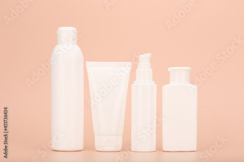 Set of white unbranded cosmetic bottles for face and body care in a row against pastel beige background. Concept of organic, natural, eco friendly cosmetics and beauty products for sensitive skin